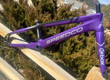 Purple Speedco bicycle frame resting outdoors on wooden rails.