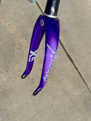 Purple bicycle fork with white decals on concrete ground.