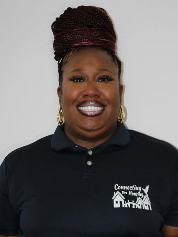 Smiling woman with braided hair in a black polo shirt with housing logo.
