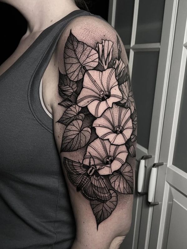 Black and white floral tattoo with a moth on an upper arm.