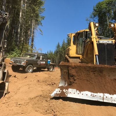 A Caterpillar bulldozer and a truck on a dirt construction site near a forest.