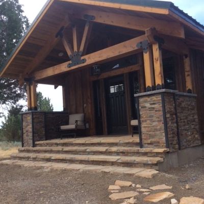Rustic wooden porch with stone pillars and steps leading to a dark wooden door.