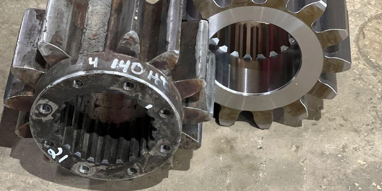 Two large metal gears, one polished and one rough, on a concrete floor.