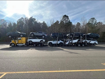 A car carrier truck loaded with multiple white and black cars on a sunny day.