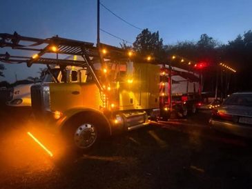 A yellow truck with orange lights parked at dusk beside other vehicles.