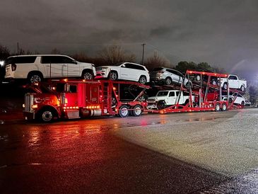 A red truck transporting multiple white vehicles at night.