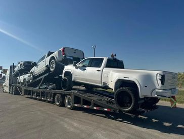 A car carrier trailer loaded with multiple white pickup trucks under a clear sky.