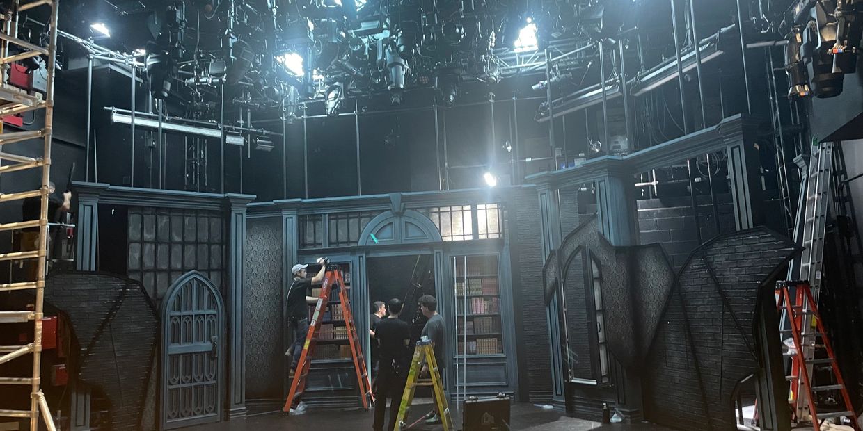Crew setting up lights on a theatrical stage with a gothic backdrop.