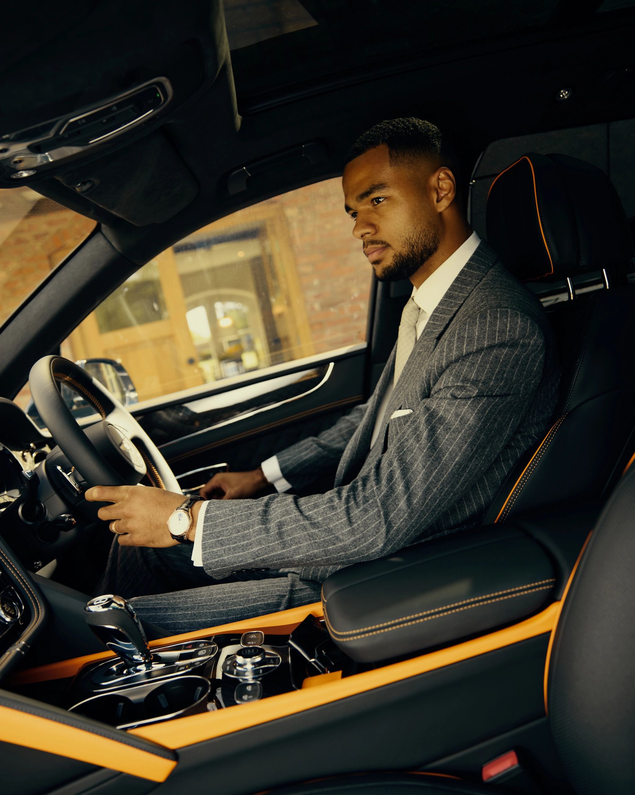 Man in a suit driving a luxury car with orange accents.