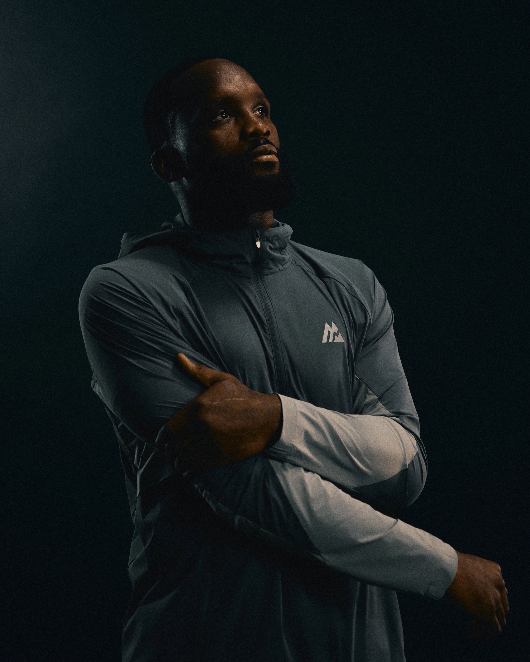 Man in a reflective jacket looks thoughtfully into the distance against a dark background.