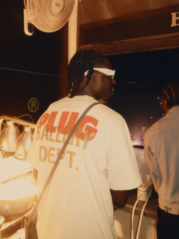 Person wearing a graphic T-shirt and white sunglasses indoors at night.