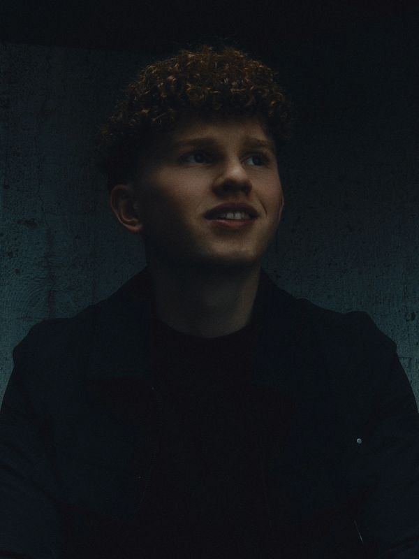 Young man with curly hair smiling in dim lighting.