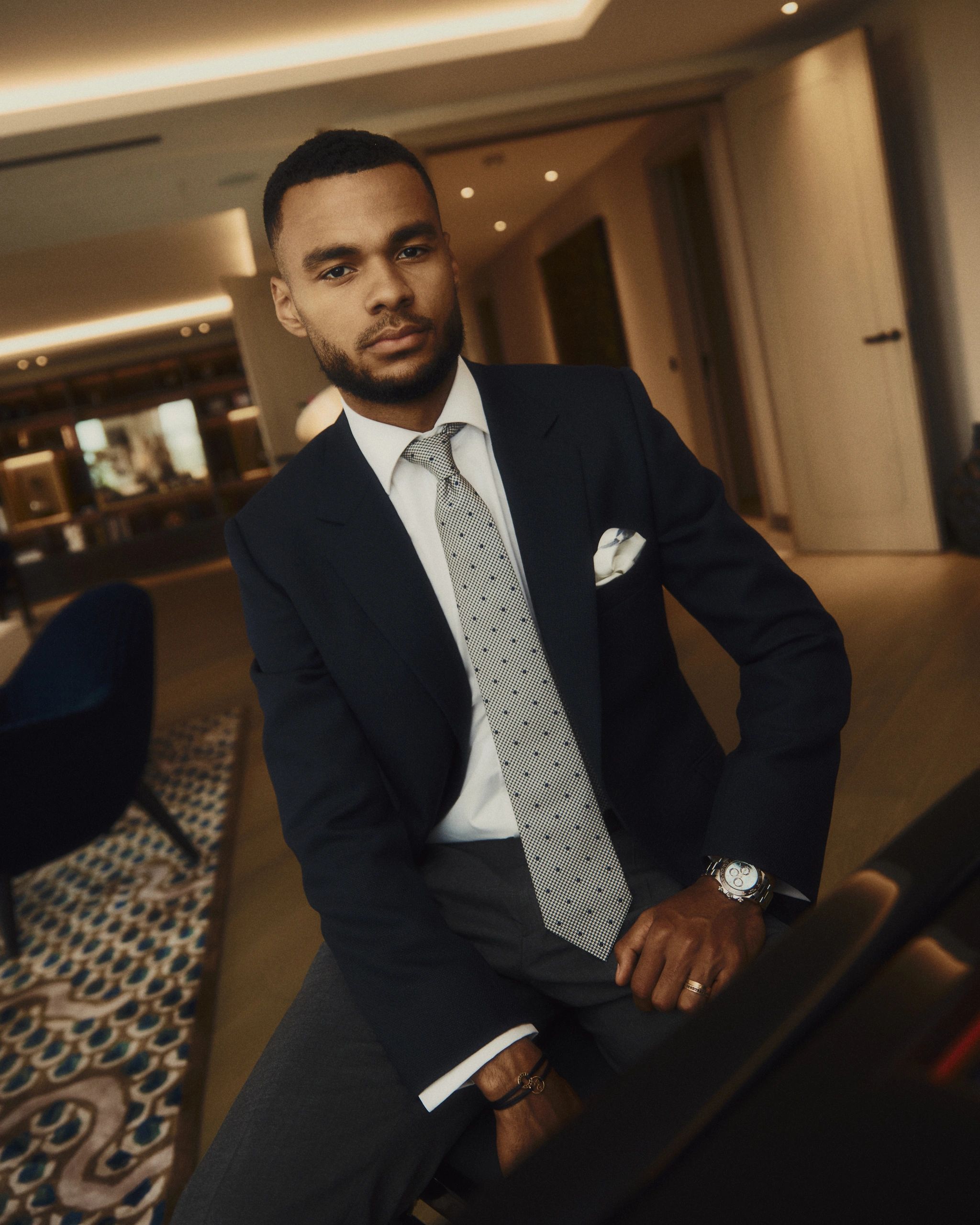 Young man in a suit sitting indoors, looking confidently at the camera.