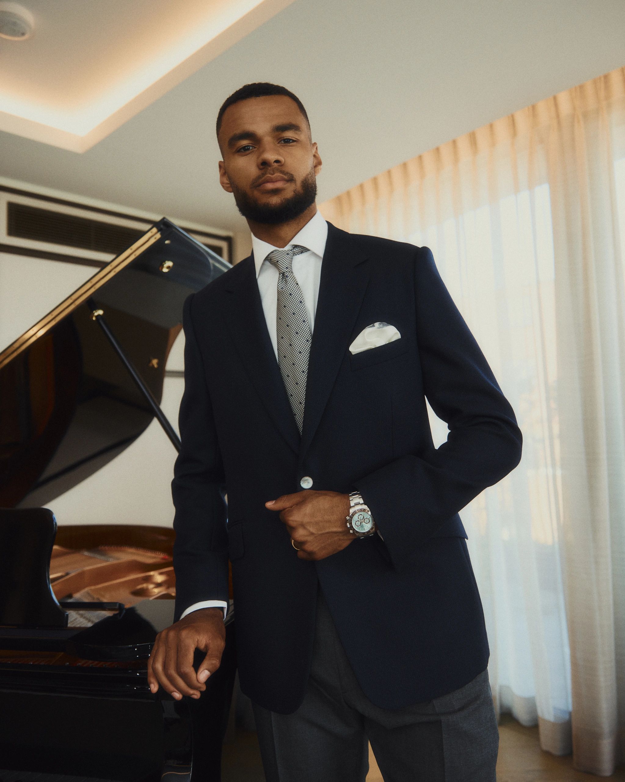 Confident man in a suit standing by a grand piano in a bright room.