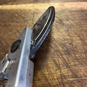 Close-up of a metal tool with a sharp blade on a wooden surface.