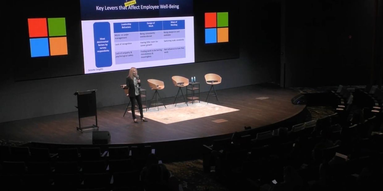 Speaker presenting on employee well-being with Microsoft logos on screen.