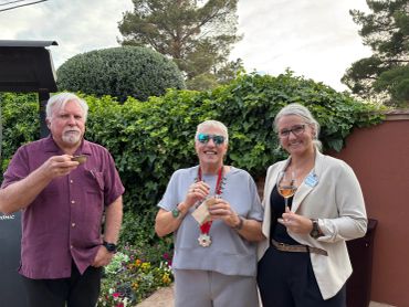 Three adults enjoying drinks outdoors by greenery.