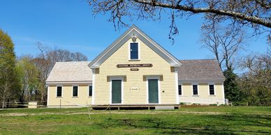 Historic yellow schoolhouse with green doors under clear blue sky.