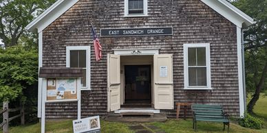 Historic wooden building labeled East Sandwich Grange with open doors and an American flag.