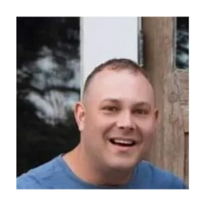 Smiling man in a blue shirt in an outdoor setting.