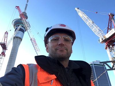 Construction worker in safety gear with cranes and a tower in the background.