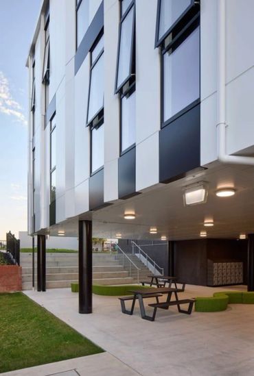 Modern building with open windows and outdoor seating under a covered area.