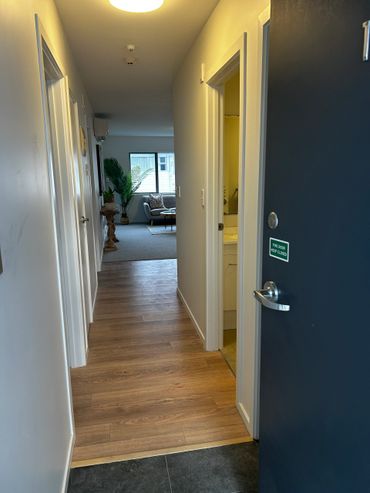 View of a modern apartment hallway leading to a living room with natural light.
