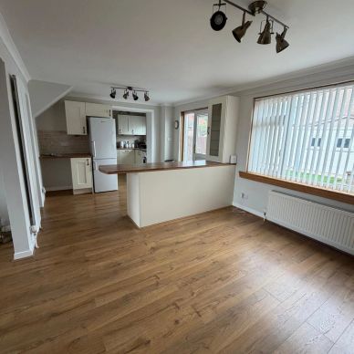 Empty kitchen and dining area with wooden flooring.