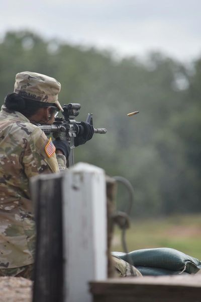 Soldier aiming and firing a rifle with a bullet casing ejecting.
