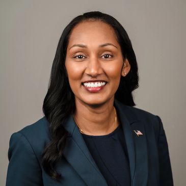 Professional woman in navy blazer with American flag pin smiling.