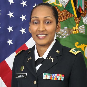 Female U.S. Army officer in uniform standing in front of American and military flags.