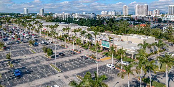 A large shopping center with parking and palm trees under a blue sky.