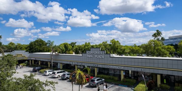 Corporate Park Plaza shopping center under a blue sky with scattered clouds.