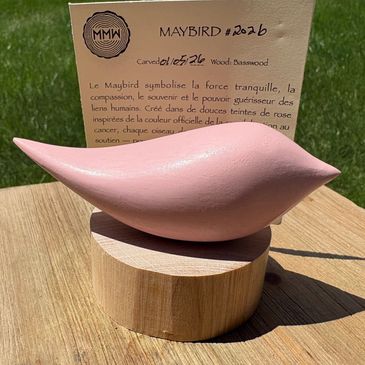 Smooth pink ceramic bird sculpture on wooden base outdoors.