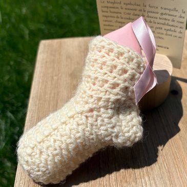 Handmade cream-colored crocheted baby sock with a pink ribbon detail.