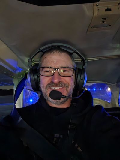 Man wearing headset and glasses, smiling inside a vehicle at night.