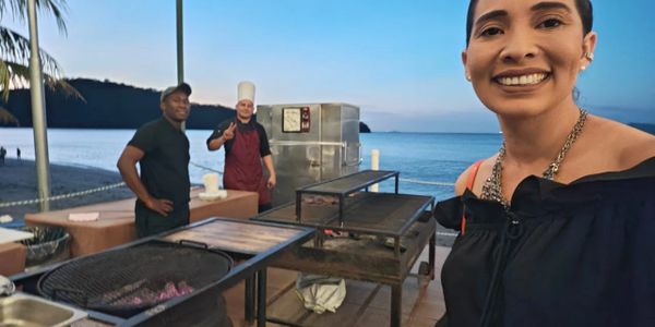 Smiling woman takes a selfie at a beachside grill with two men in the background.