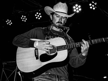 Chris Matthews playing guitar and harmonica onstage.