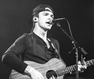 Max Goen singing on stage with a guitar.