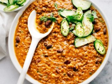 Hearty lentil and bean curry garnished with cucumbers and herbs.