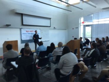 A speaker presenting to an audience in a modern conference room.