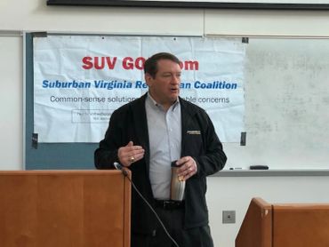 Man speaking at a podium in front of a Suburban Virginia Republican Coalition banner.