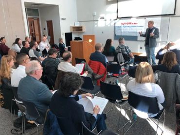 A speaker presents to an engaged audience in a bright conference room.