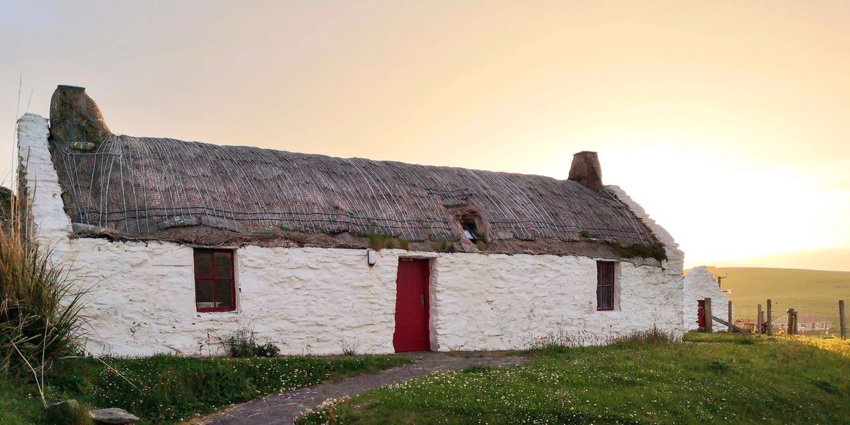 White cottage with thatched roof at sunset.