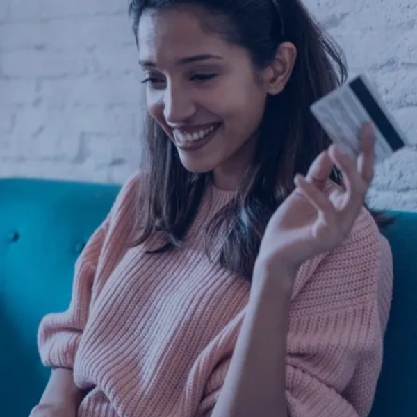 Smiling woman holding a credit card, sitting on a blue couch.