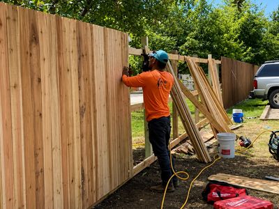 A worker installs wooden fence panels outdoors on a sunny day.