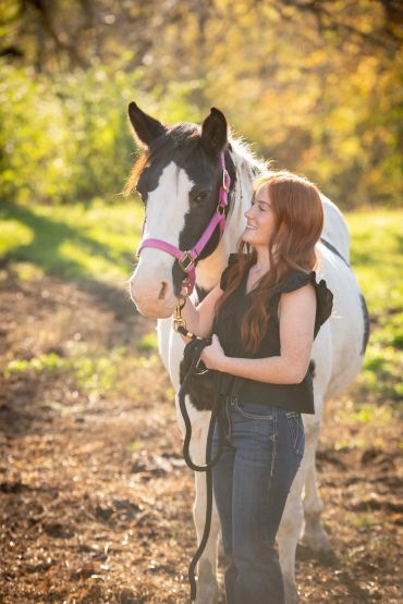 Young woman with a black and white horse outdoors.