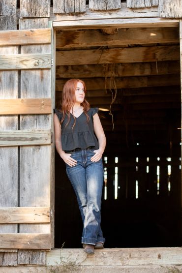 Woman standing in a barn doorway looking outside.
