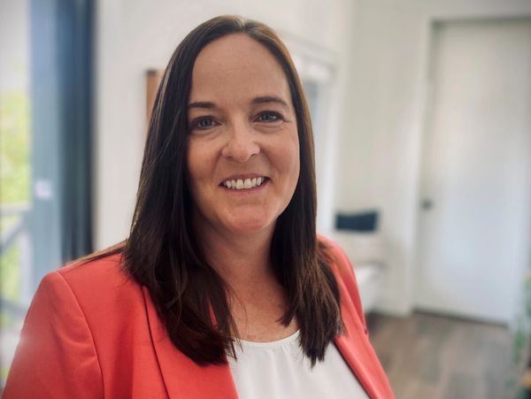 Smiling woman in an orange blazer and white top indoors.