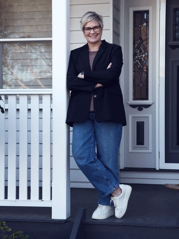 Smiling woman with glasses leaning on a porch post.